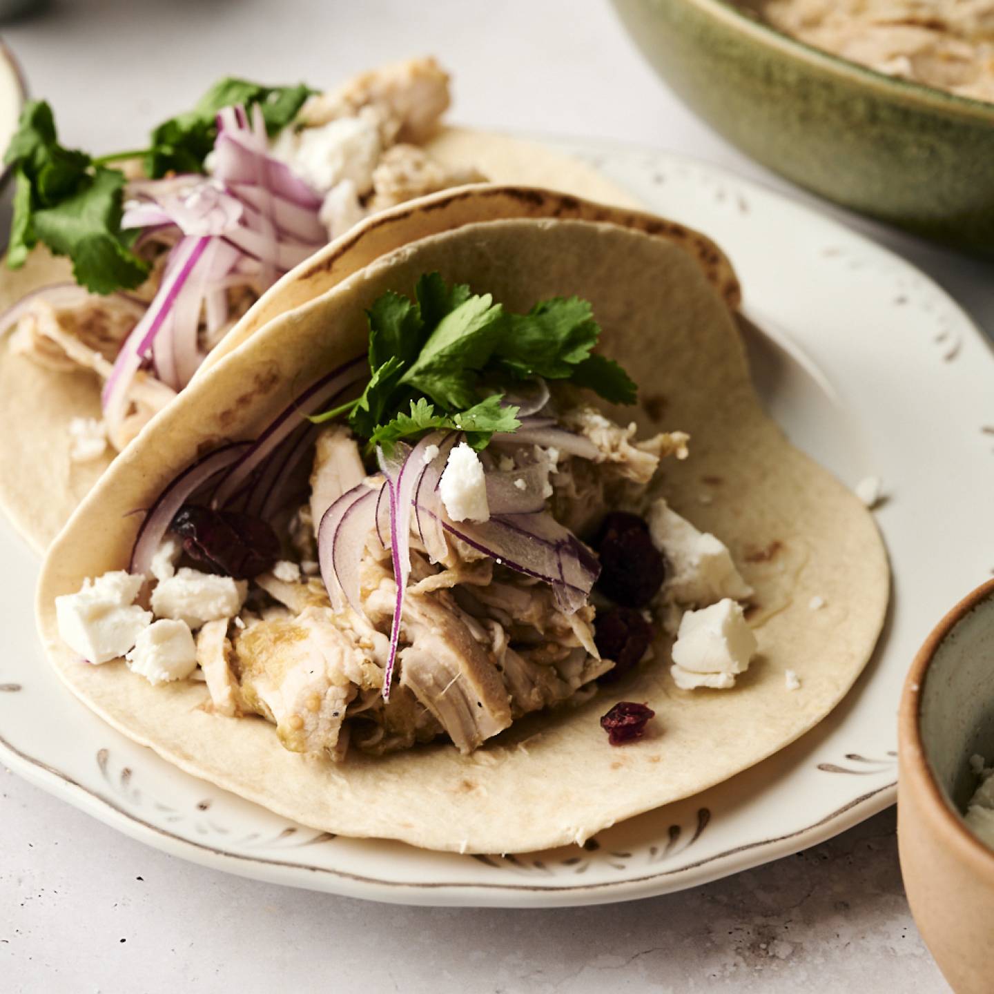 Shredded turkey tacos with red onion, cilantro, dried cranberries, and crumbled cheese on soft flour tortillas.