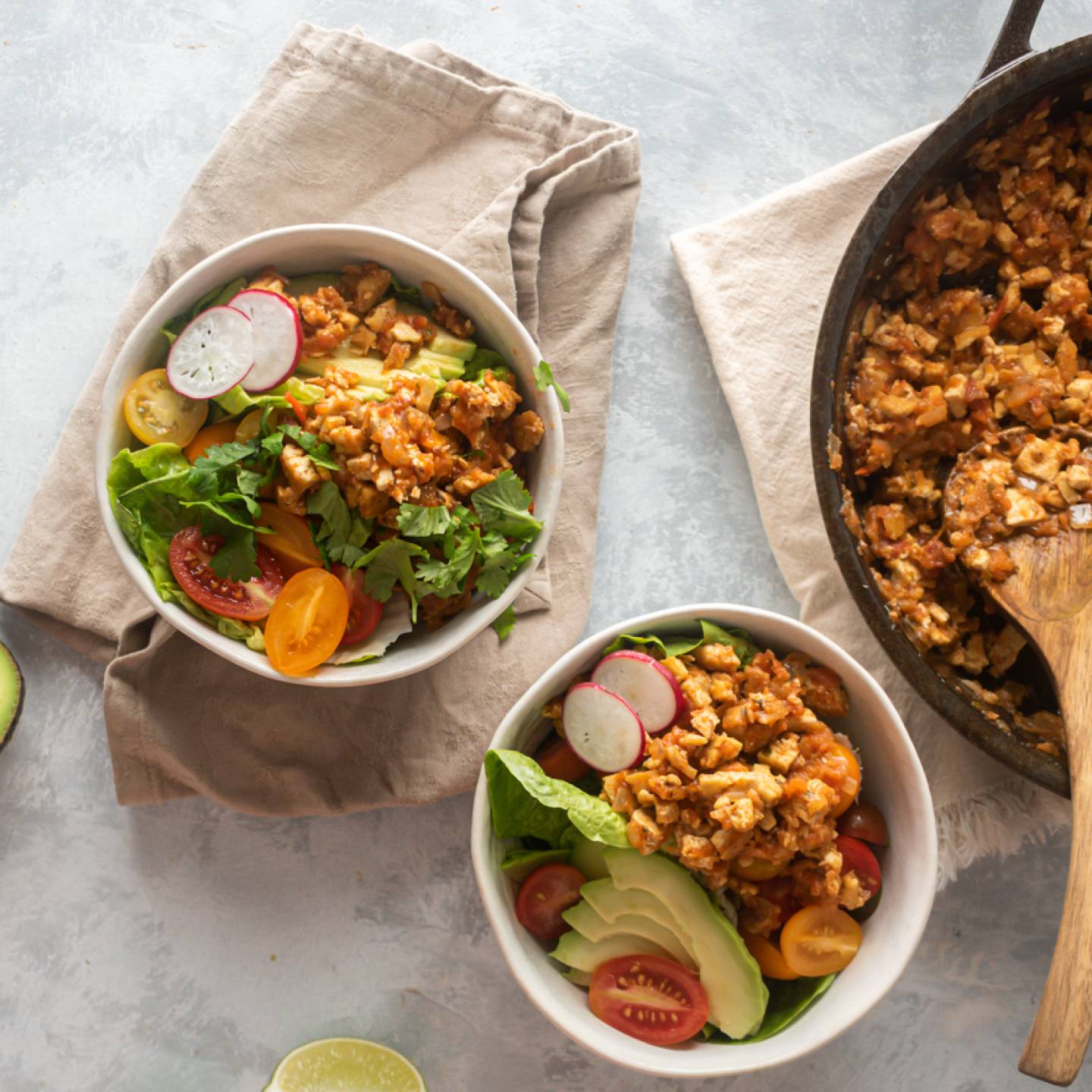 Chipotle Sofritas tofu in a skillet and served in bowls with lettuce, avocado, tomato, and cilantro.