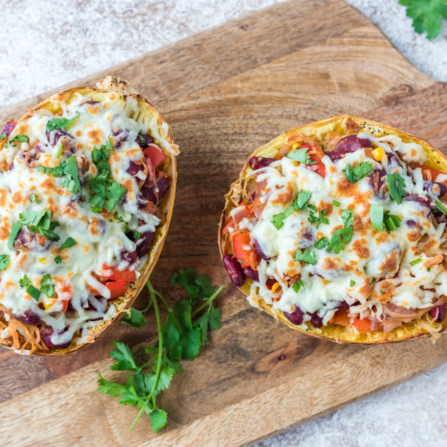 Spaghetti squash burrito bowls with beans, peppers, onions, seasoning, and melted cheese on a cutting board.