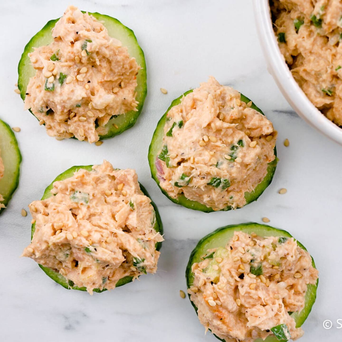 Spicy tuna salad on cucumber slices with sesame seeds.