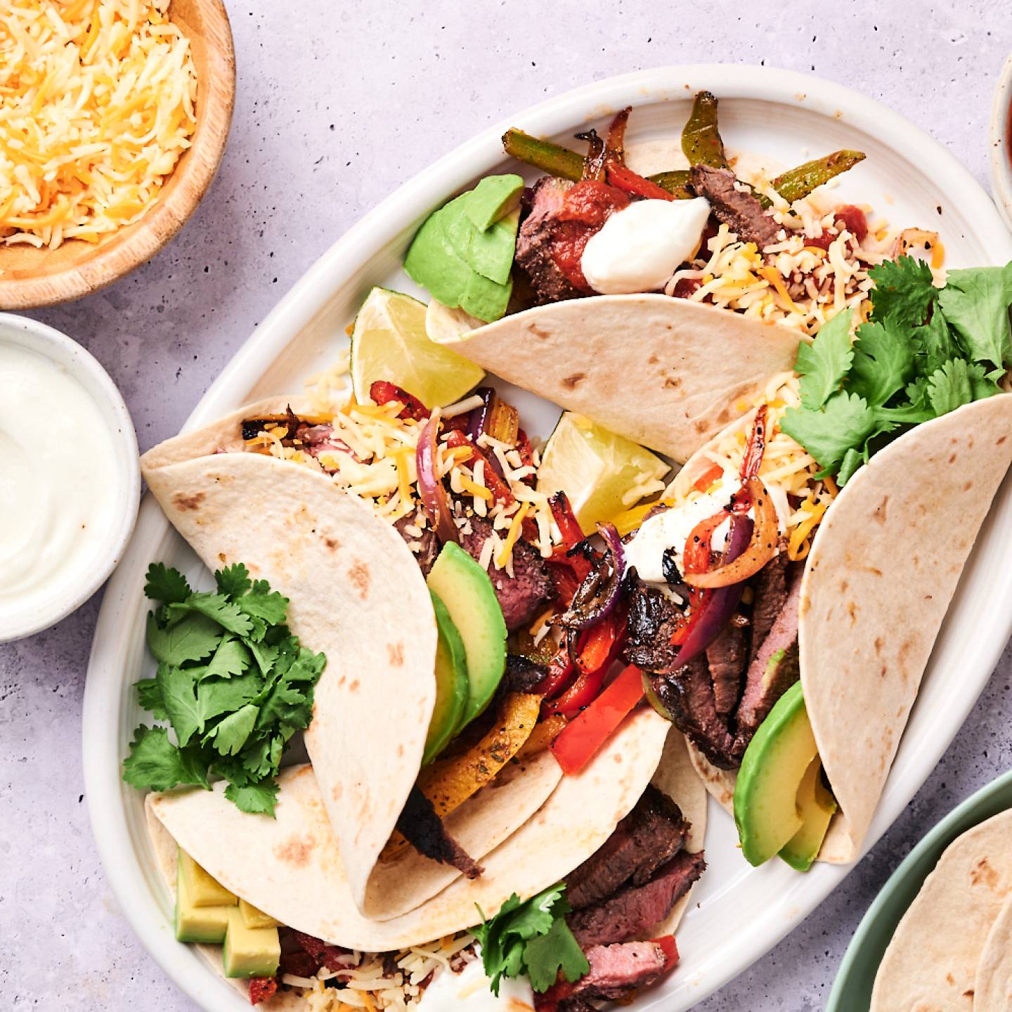 Steak fajitas with bell peppers, red onion, tender steak, sour cream, cheese, avocado, and cilantro in flour tortillas.