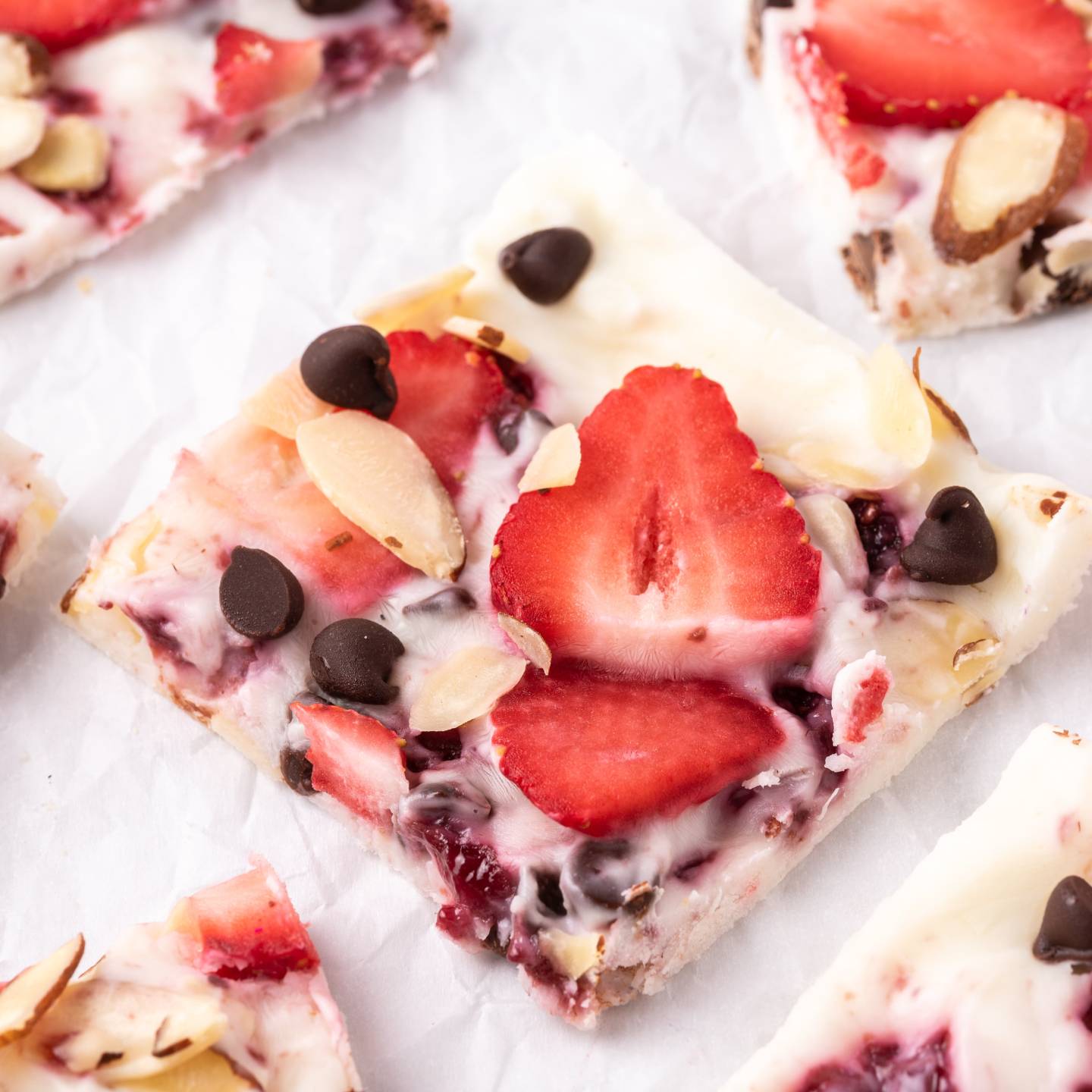 Strawberry frozen yogurt bark with chocolate chips, sliced almonds, and raspberry jelly broken into squares.