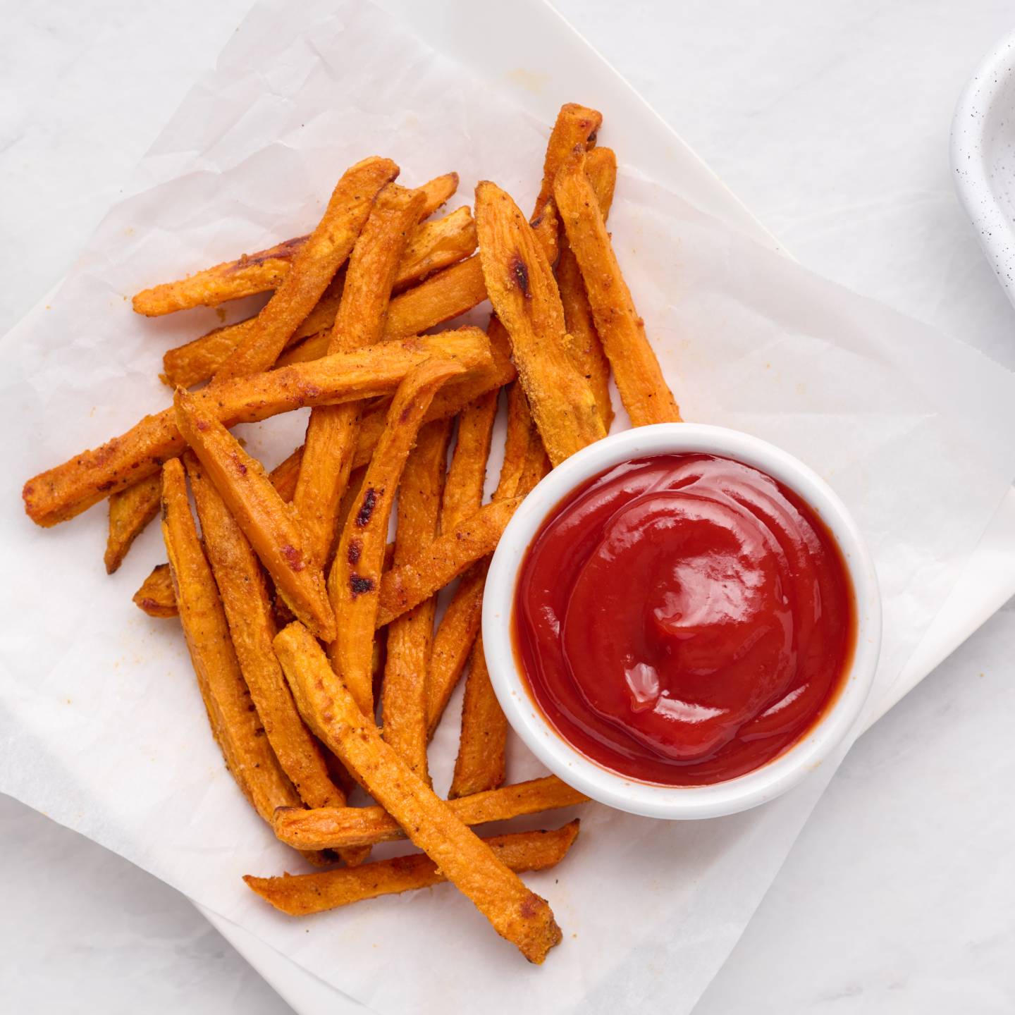 Baked sweet potato fries with a crispy exterior on a plate with ketchup.