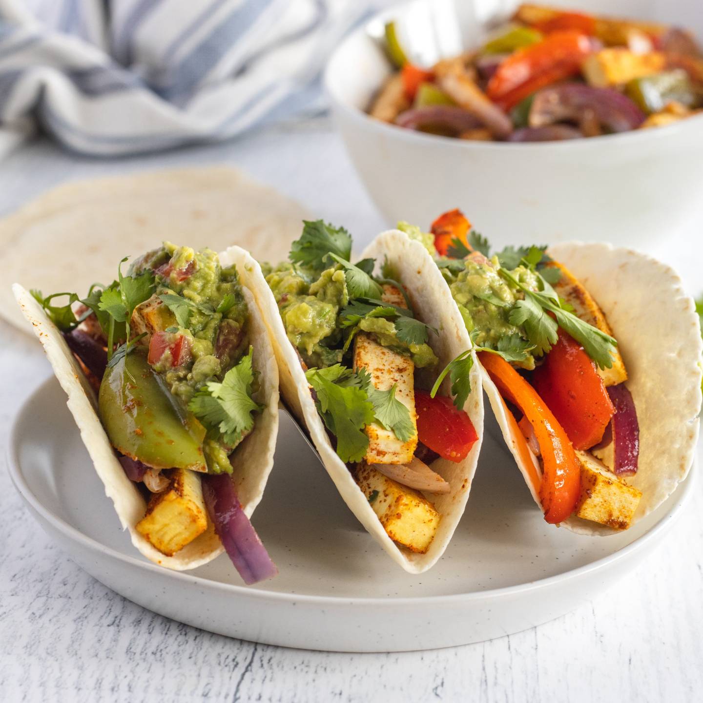 Tofu fajitas with extra firm tofu, red bell peppers, green bell peppers, and red onions cooked in spices served in flour tortillas with guacamole.