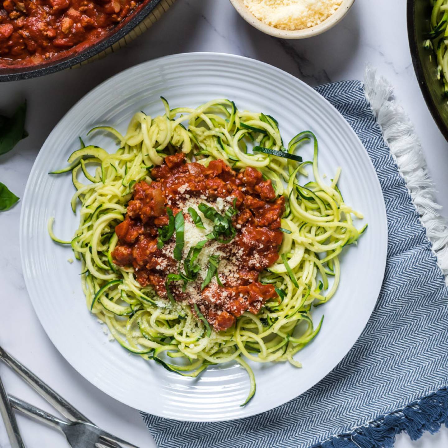 Tomato basil zucchini noodles with ground turkey served on a plate with basil and Parmesan cheese.