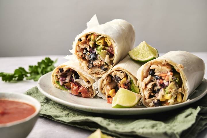 A plate of fresh and flavorful Fish Burritos, packed with black beans, corn, avocado, cabbage slaw, and juicy seasoned fish, wrapped in soft tortillas and served with lime wedges. 