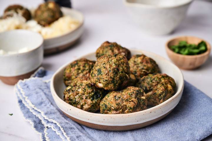 Spinach meatballs made with ground beef served on a plate with spinach and Parmesan cheese on the side.