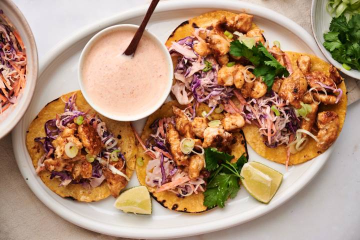 Bang bang chicken tacos served on warm corn tortilla with crunchy cabbage slaw, cilantro, lime wedges, and green onions.