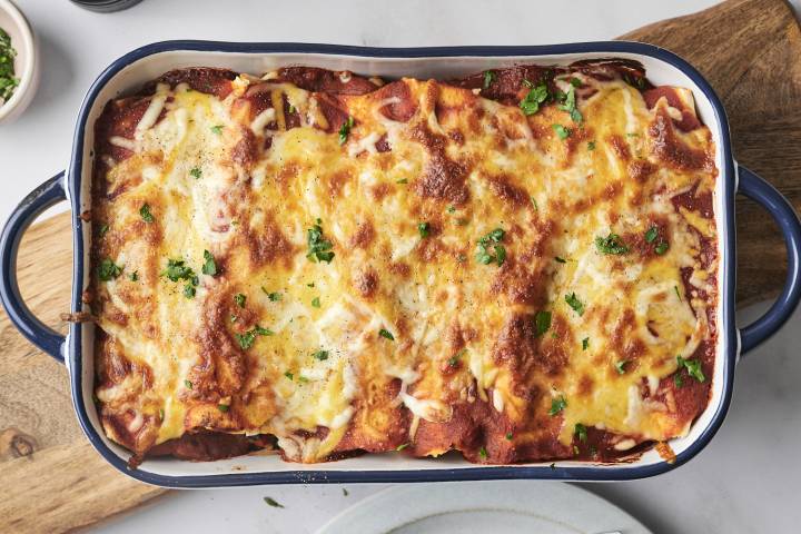 The freshly baked breakfast enchiladas are topped with melted cheese and garnished with fresh parsley. The dish is golden and bubbly from the oven.