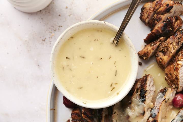 Gravy in a bowl with sliced turkey off to the side.