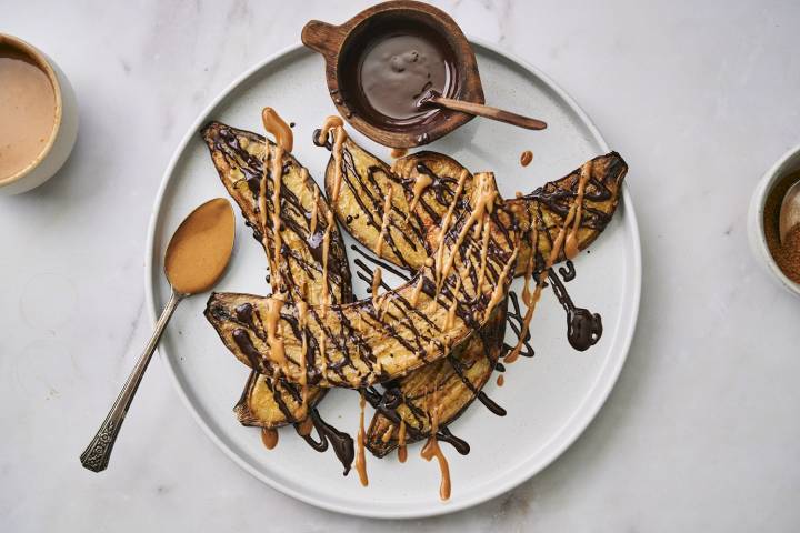 Grilled bananas on a plate with peanut butter, chocolate, and cinnamon. 