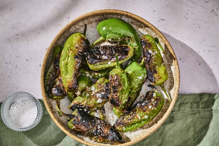 Grilled shishito peppers with blistered, charred edges served in a bowl with sea salt.