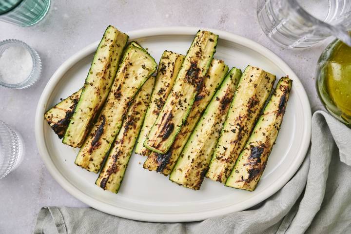 Grilled zucchini spears with dark grill marks served on a platter with olive oil, salt, pepper, and garlic.