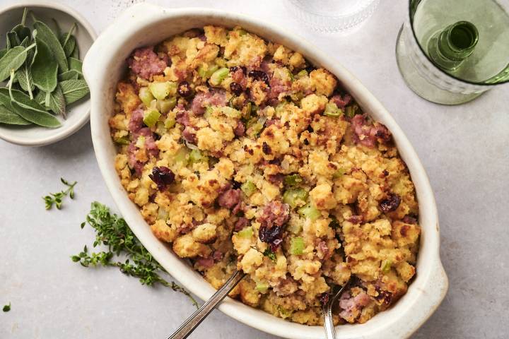 Healthy cornbread stuffing with sausage, celery, and dried cranberries  in baking dish with spoons ready to serve.