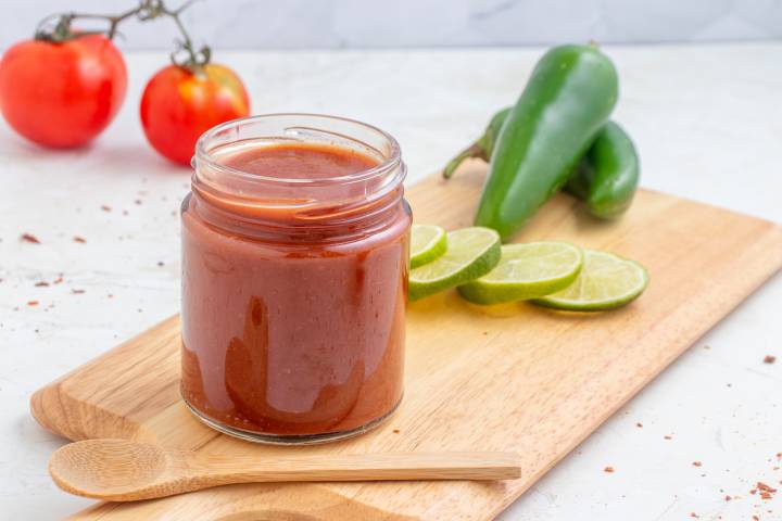 Homemade taco sauce made with tomato sauce, vinegar, spices, and sugar in a glass jar on a cutting board.
