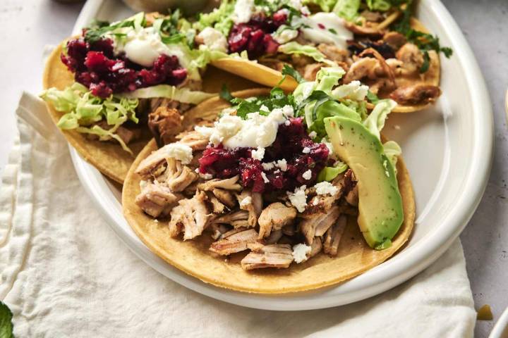 Leftover turkey tacos with cranberry relish, cilantro, avocado, and queso fresco being served on a plate.