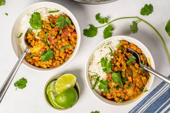 Bowls of lentil coconut curry served over white rice, garnished with fresh cilantro and lime wedges.