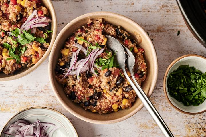 Bowls of cooked Mexican quinoa topped with fresh red onion slices and chopped cilantro, ready to be served with additional toppings on the side.