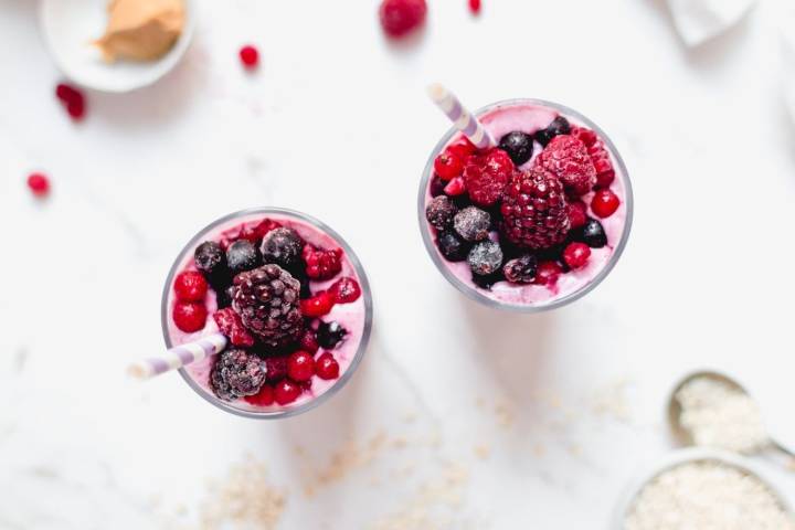 A vibrant banana berry smoothie topped with frozen mixed berries.