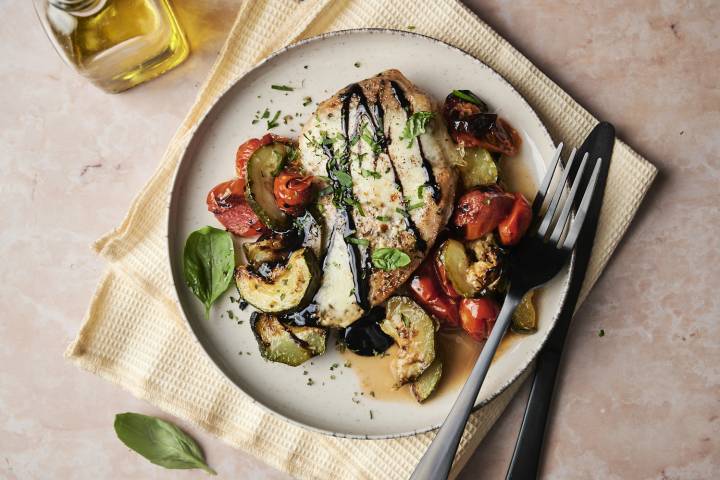 A plate of caprese chicken with roasted zucchini and tomatoes, topped with balsamic glaze and fresh basil.