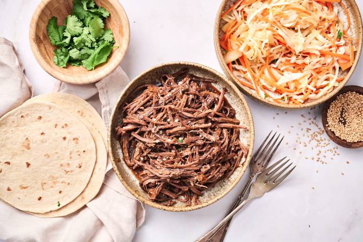 Slow cooker Korean beef tacos with corn tortillas, coleslaw, hot sauce, and Sriracha.