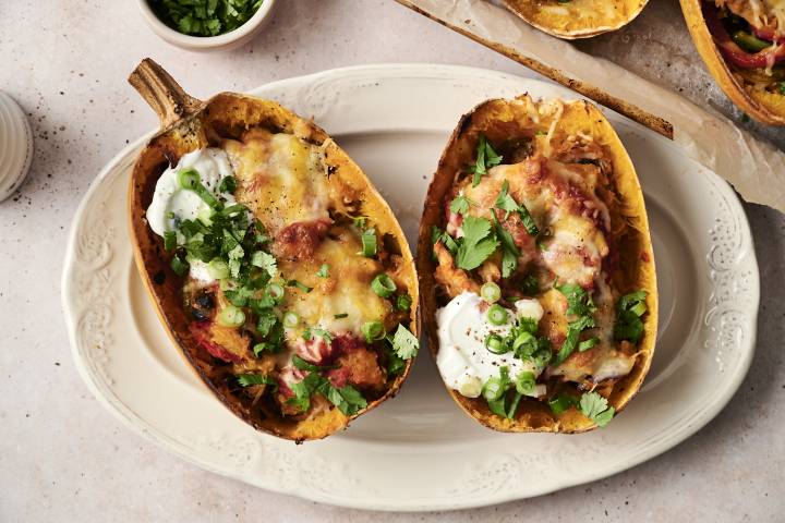 Two spaghetti squash enchilada boats topped with melted cheese, sour cream, green onions, and cilantro on a white plate.