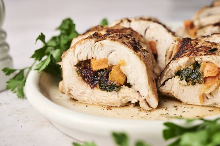 Stuffed turkey tenderloin with sweet potatoes, spinach, and dried cranberries sliced and served on a plate with parsley. 