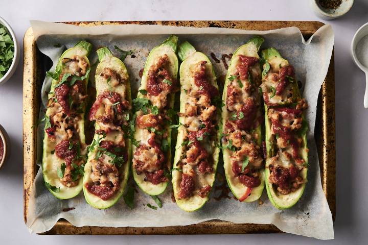 Baked Tex-Mex stuffed zucchini with cheese, tomato sauce, and cilantro on a parchment-lined baking tray.