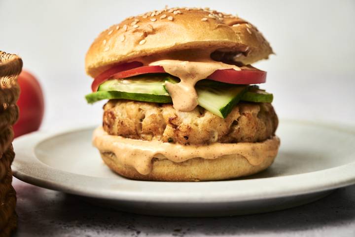 Tilapia fish burger with sauce cucumber and tomato on a sesame seed bun.