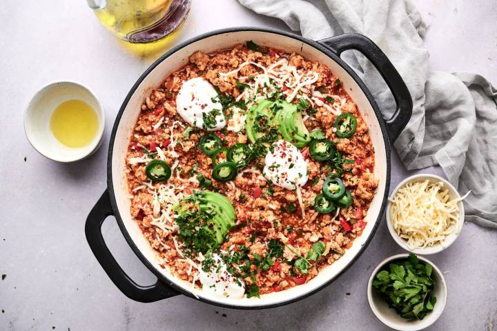 A skillet filled with turkey taco cauliflower rice, topped with avocado, jalapeños, sour cream, shredded cheese, and fresh cilantro.