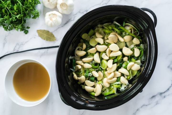 Leeks, onions, and whole garlic cloves in a low cooker.