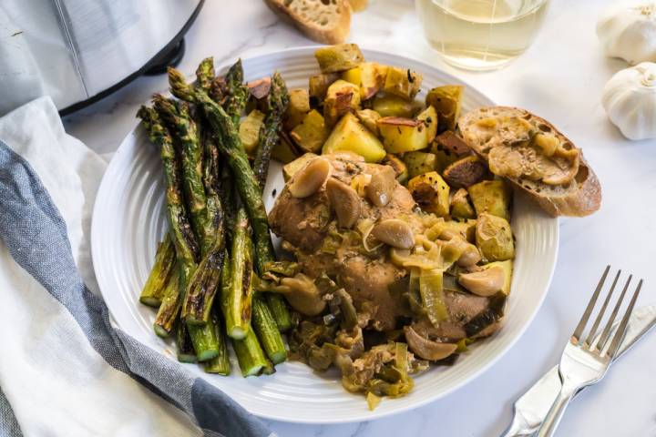 Cooked chicken with 40 cloves of garlic on a plate with asparagus and potatoes.