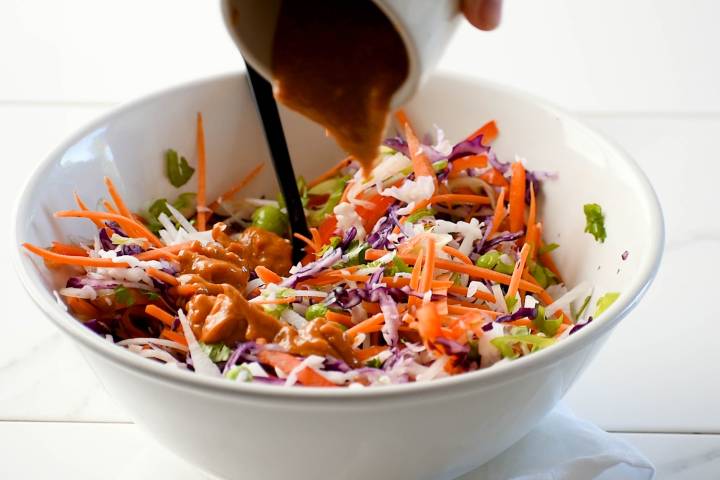 Cabbage slaw, carrots, edamame, cilantro, jicama, and peanut dressing in a bowl.