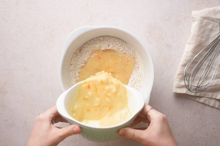 Eggs, milk, and bananas being added to a bowl of flour for pancakes.