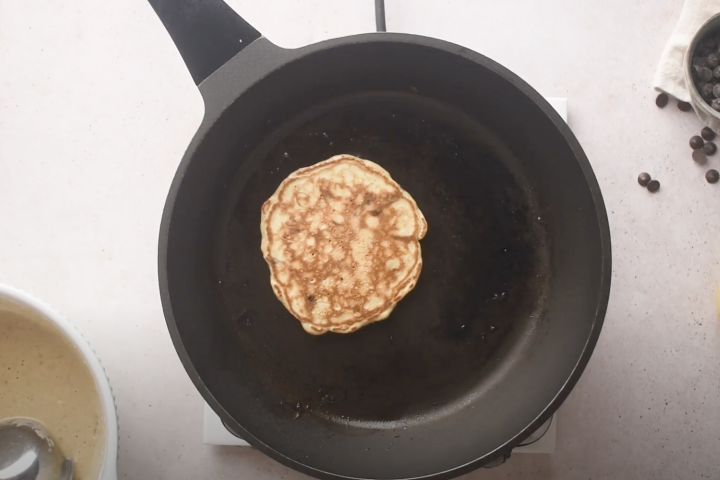 Banana chocolate chip pancakes cooking in a skillet.