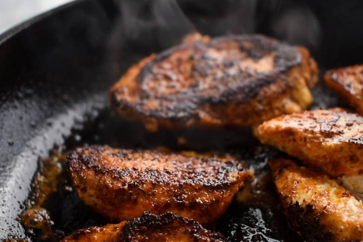 Chicken breast covered in spices being blackened in a skillet with butter.