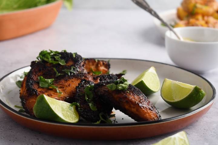 Blackened chicken breast on a plate with limes.