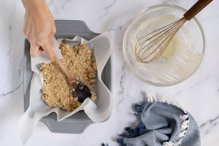 Oatmeal bar dough being pressed into a baking sheet with parchment paper.