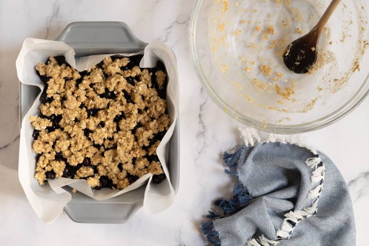 Blueberries and oatemal topping being added to a baking dish.