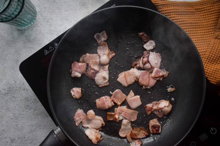 Bacon being cooked in a skillet until crispy.