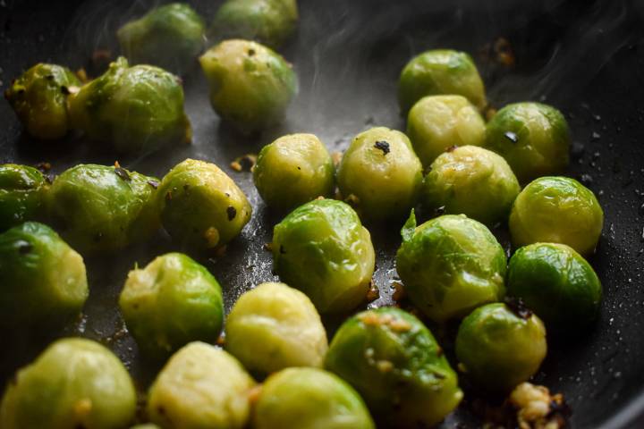 Brussels sprouts cooking in a skillet with red pepper flakes and garlic.