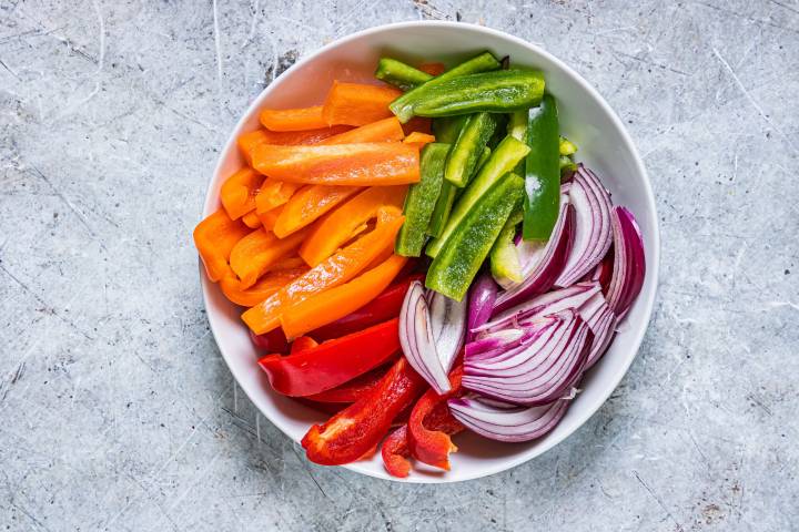 Sliced bell peppers and red onions in a white bowl.