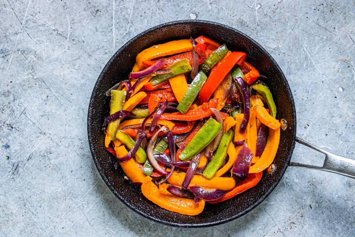 Cooked fajita veggies in a skillet including bell peppers and onions.