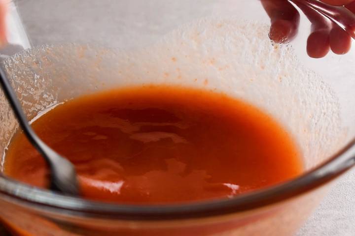 Clamato juice, lime juice, and ketchup being stirred in a bowl.