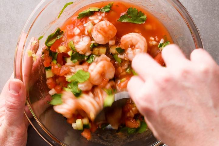 Shrimp, onion, and cucumber being adding to Mexican shrimp cocktail sauce.