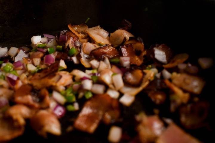 Bacon, jalapenos, and red onion cooking in a skillet.