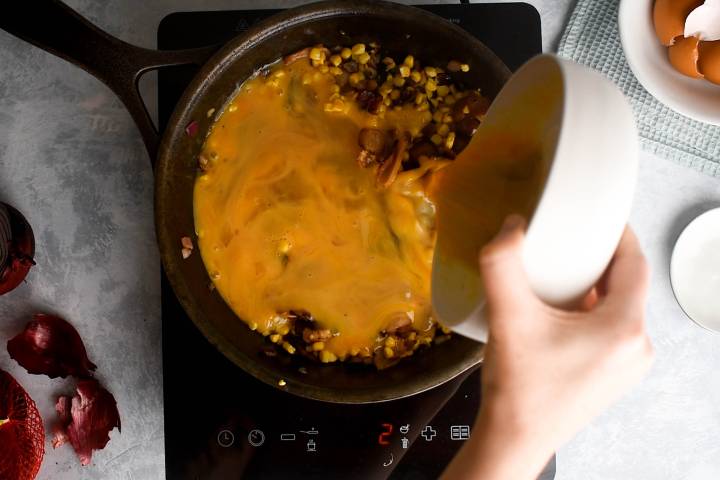 Eggs being adding to a corn and bacon frittata.