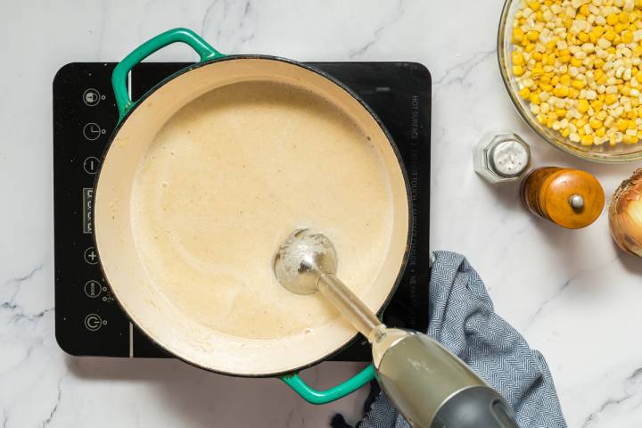 Cauliflower being blended into soup with an immersion blender.