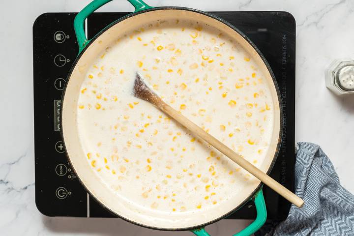 Corn chowder with fresh corn in a large soup pot with a wooden spoon.