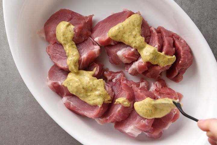 Pork chops being coated with a mustard thyme sauce.